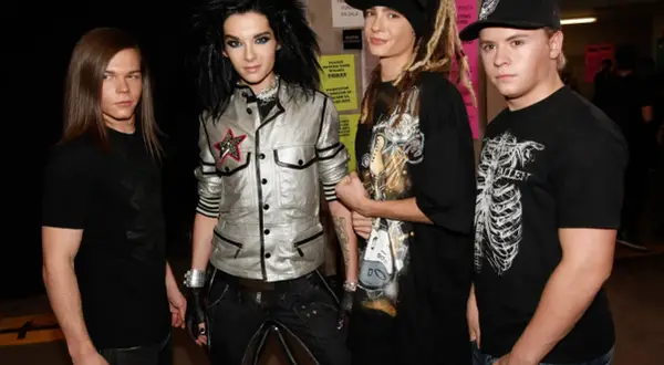 Członkowie Tokio Hotel pozują do zdjęcia. Bill Kaulitz w błyszczącej kurtce, Tom Kaulitz w czapce i z dredami, a obok nich Georg Listing i Gustav Schäfer.