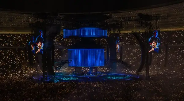 Koncert Dawida Podsiadło, tłum z zapalonymi światłami, wielkie ekrany z wizerunkiem artysty.