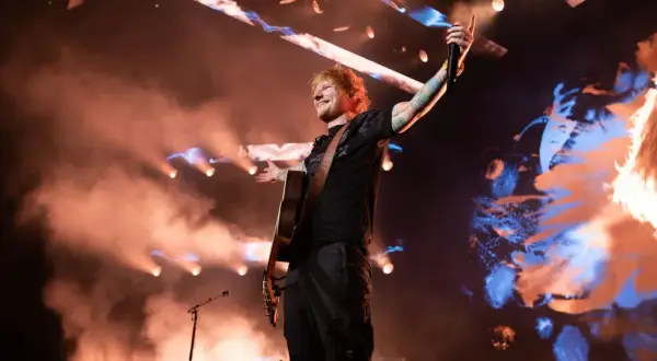 Ed Sheeran w Polsce, na scenie z gitarą, w otoczeniu dymu i świateł, pozdrawia publiczność.