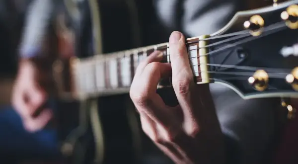 Dłoń grająca akord na gitarze. Muzyka tworzy niepowtarzalny zespół z korą drzewa, z którego wykonano instrument.