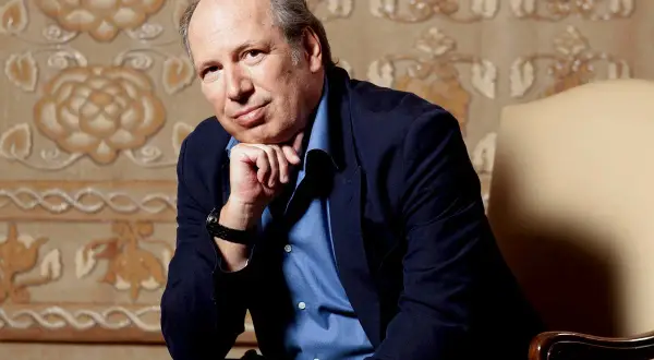 Hans Zimmer, kompozytor znany z muzyki do filmów, siedzi w fotelu, opierając podbródek na dłoni.