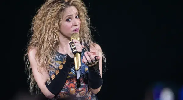 Shakira, znana z latynoskiego pochodzenia, śpiewa na scenie z mikrofonem w dłoni.