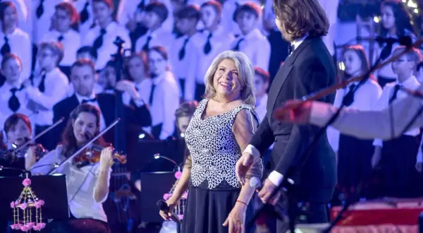 Krystyna Prońko na scenie, uśmiechnięta, w otoczeniu chóru i orkiestry. Jej utwory brzmią pięknie.