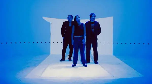 Trzy osoby stoją na scenie oświetlonej na niebiesko, tworząc atmosferę idealną do shoegaze.