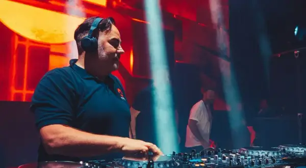 DJ Kris w akcji, miksuje muzykę na żywo. W tle pulsujące światła i tłum.