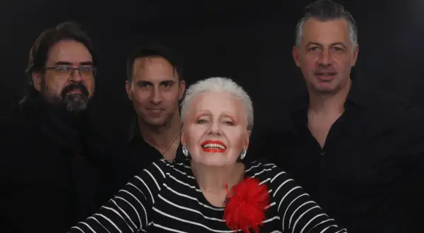 Edek Tango i jego zespół w czerniach, gotowi na występ. Wokalistka z czerwoną broszką błyszczy na pierwszym planie.