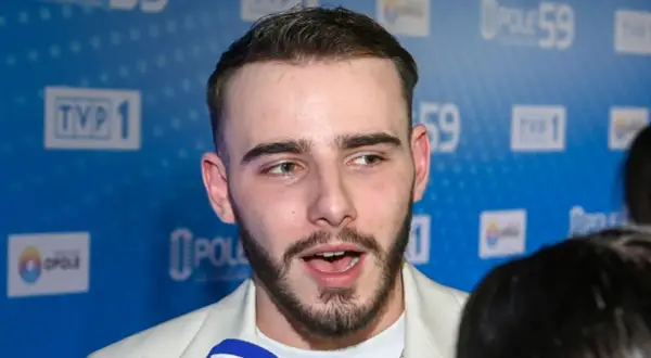 Krystian Ochman, z żoną u boku, pozuje na tle niebieskiej ścianki z logo TVP 1 i Opole 59.