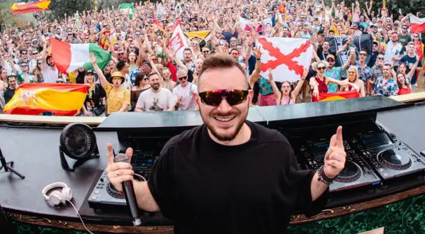 Skytech DJ w akcji, rozkręca tłum na festiwalu. W tle widać flagi i radosnych ludzi.