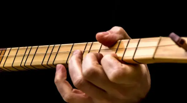 Dłoń na gryfie gitary, palce dociskają struny. Idealny moment, by dowiedzieć się, jak nastroić gitarę.