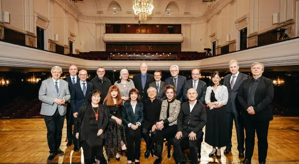 Uczestnicy międzynarodowego konkursu pianistycznego im. Fryderyka Chopina pozują do wspólnego zdjęcia w eleganckiej sali koncertowej.