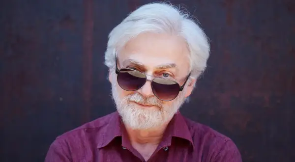 Krystian Zimerman w okularach przeciwsłonecznych, z siwą brodą i włosami, w bordowej koszuli.