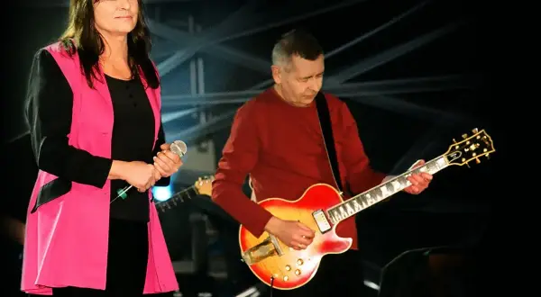 Kobieta z mikrofonem i mężczyzna grający na gitarze, członkowie zespołu Breakout, na scenie.