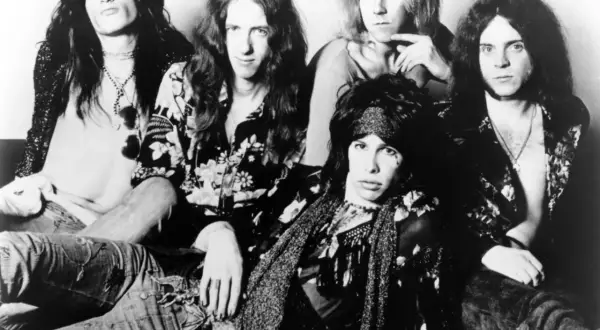 Aerosmith członkowie w rockowym stylu, z długimi włosami i charakterystycznymi strojami.