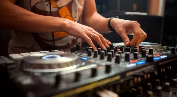 Dłonie DJ-a miksujące muzykę na sprzęcie. Widać pierścionek na palcu i zegarek. To polscy DJ-e tworzą rytm.