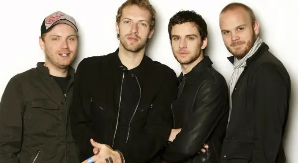 Członkowie Coldplay pozują do zdjęcia. Na dłoni jednego z nich widnieje tatuaż symbolizujący pauzę.