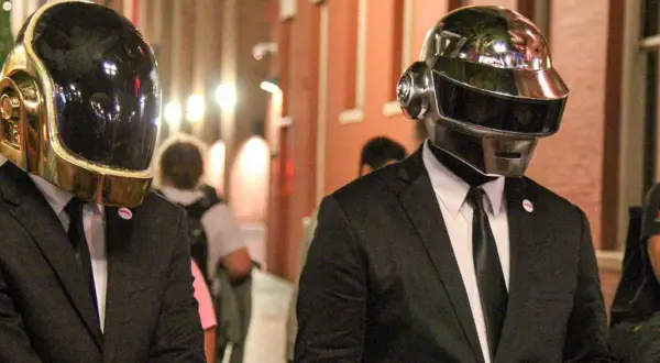 Daft Punk członkowie w złotych i srebrnych hełmach, ubrani w garnitury, idą ulicą.