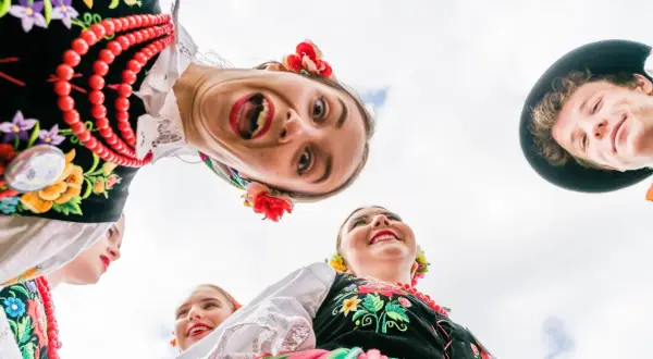 Uśmiechnięci młodzi ludzie w barwnych strojach ludowych, celebrujący polski folklor.