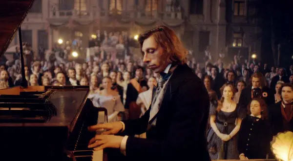 Młody pianista, jakby uczeń Chopina, gra na fortepianie przed zgromadzoną publicznością w historycznym stroju.