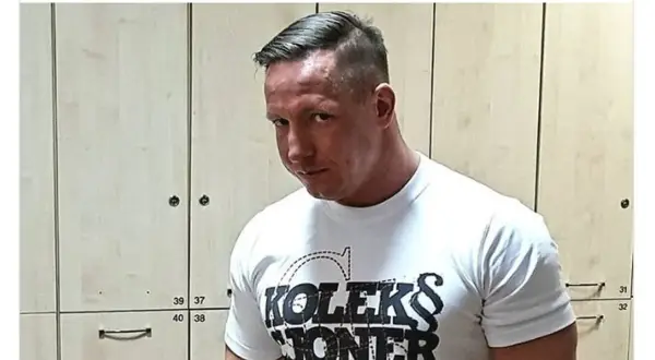 Tomasz Chada w białej koszulce z napisem "KOLEKS JONER ARZUTOW", pozuje na tle szafek.