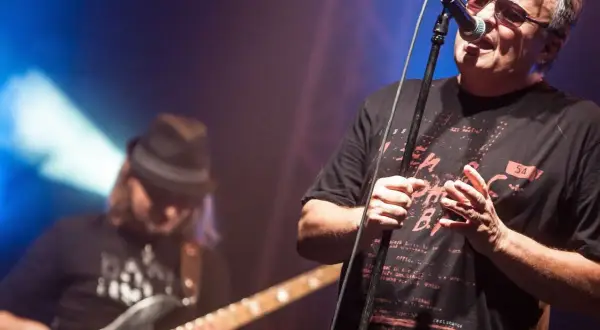 Wokalista Budki Suflera śpiewa na koncercie. W tle basista gra na gitarze. Piosenki Budki Suflera alfabetycznie to ich bogaty repertuar.