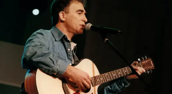 Seweryn Krajewski na scenie, gra na gitarze i śpiewa do mikrofonu. Jego muzyka wciąż porusza serca, a pytanie "czy Seweryn Krajewski żyje" jest niepotrzebne, bo jego twórczość jest wieczna.