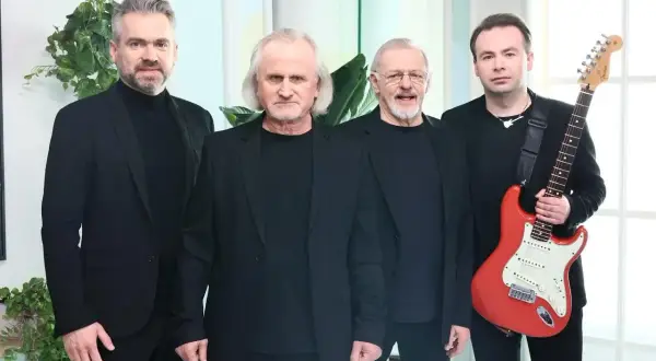 Czterech mężczyzn w czarnych strojach. Jeden z nich trzyma czerwoną gitarę.