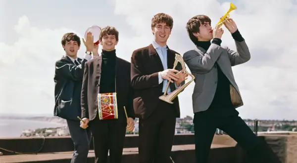 The Beatles w swoich eleganckich garniturach, grając na instrumentach, tworzą radosną atmosferę, jakby zapowiadali nowe utwory.