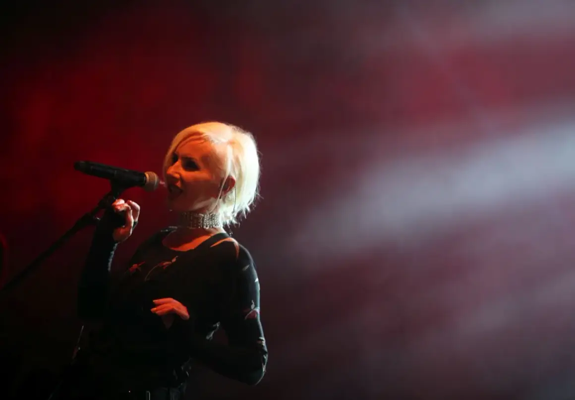 Kora Jackowska śpiewa na scenie, wykonując swoje utwory. Wokół niej unosi się mgła, a czerwone światła tworzą nastrojową atmosferę.
