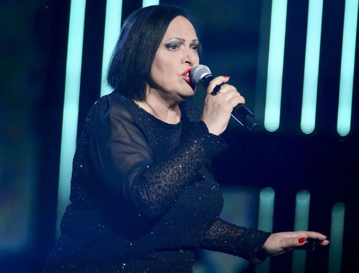 Grażyna Łobaszewska śpiewa swoje utwory na scenie, ubrana w błyszczącą, czarną suknię.