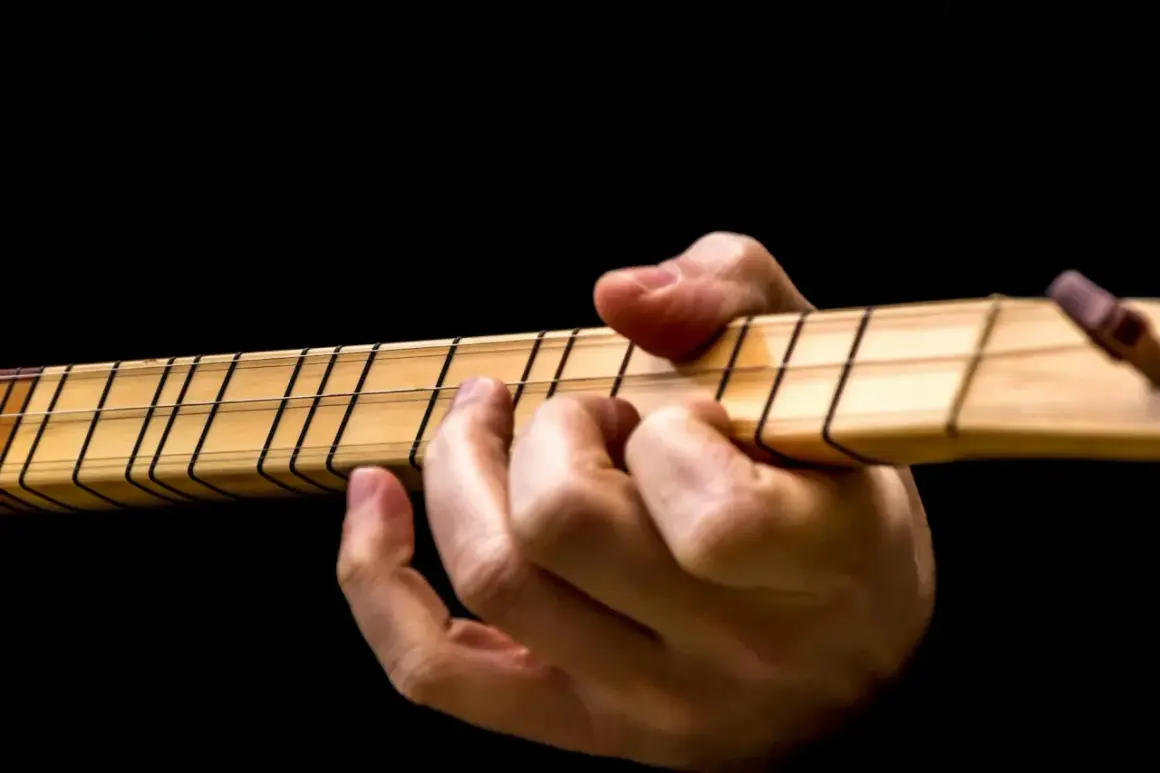Dłoń na gryfie gitary, palce dociskają struny. Idealny moment, by dowiedzieć się, jak nastroić gitarę.