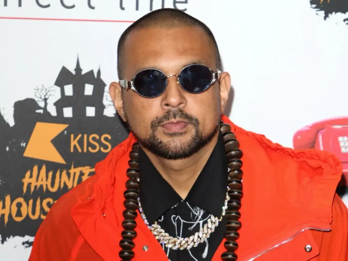 Sean Paul w pomarańczowej kurtce i okularach, gotowy do wykonania swoich hitowych sean paul utwory.