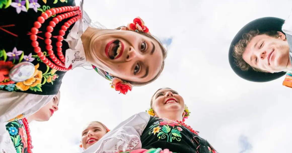 Uśmiechnięci młodzi ludzie w barwnych strojach ludowych, celebrujący polski folklor.