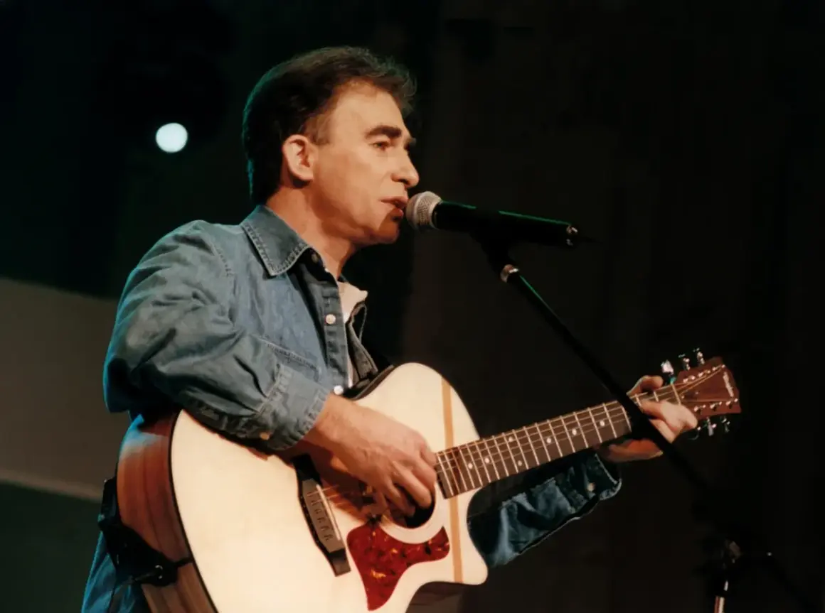 Seweryn Krajewski na scenie, gra na gitarze i śpiewa do mikrofonu. Jego muzyka wciąż porusza serca, a pytanie "czy Seweryn Krajewski żyje" jest niepotrzebne, bo jego twórczość jest wieczna.