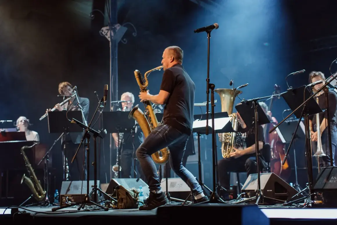 Koncert z utworami Krzysztofa Pendereckiego. Saksofonista w centrum, w tle orkiestra dęta i instrumenty smyczkowe.