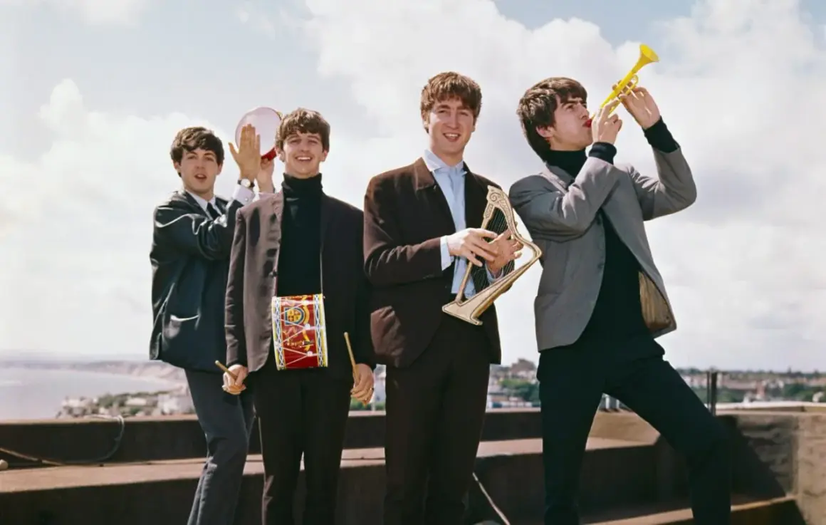 The Beatles w swoich eleganckich garniturach, grając na instrumentach, tworzą radosną atmosferę, jakby zapowiadali nowe utwory.