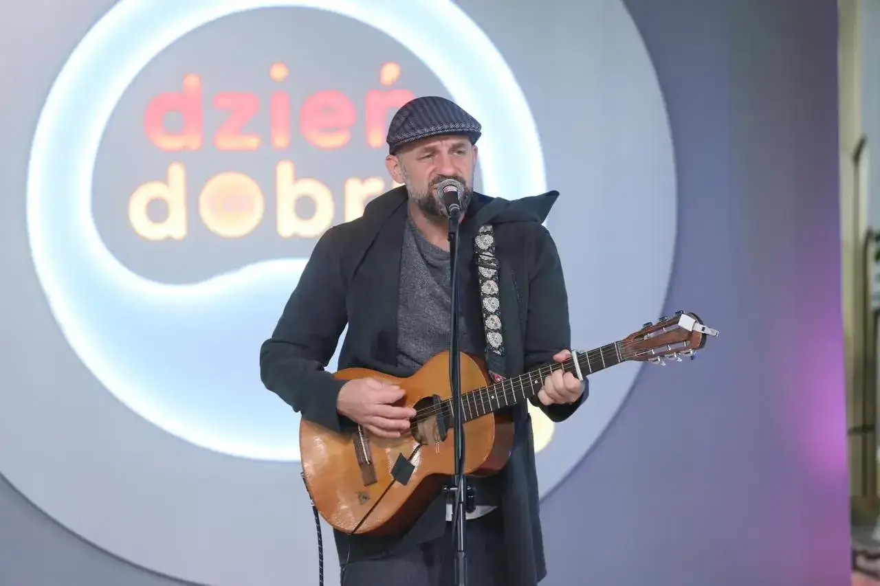Skubas w czapce i płaszczu gra na gitarze. W tle logo
