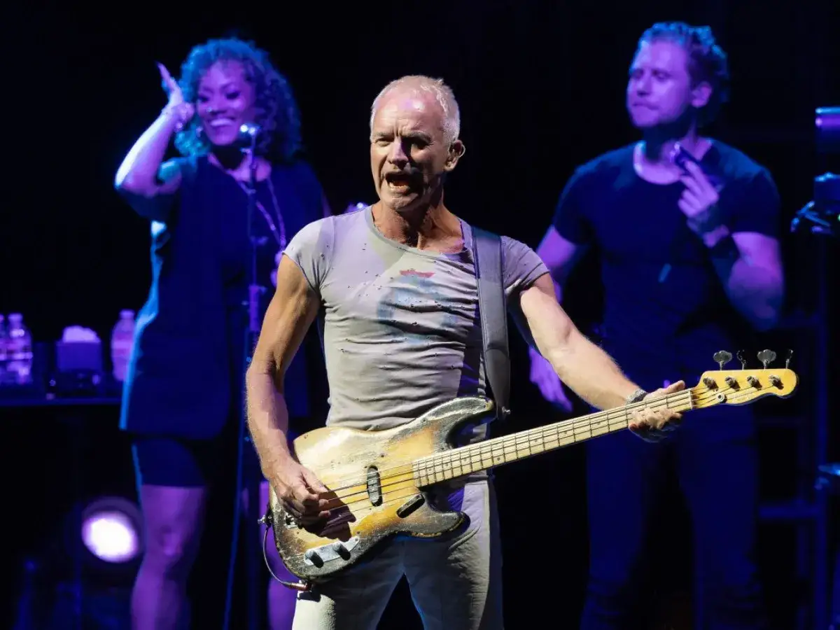 Sting gra na gitarze basowej, a za nim wokalistka i gitarzysta. Koncert zespołu Sting.