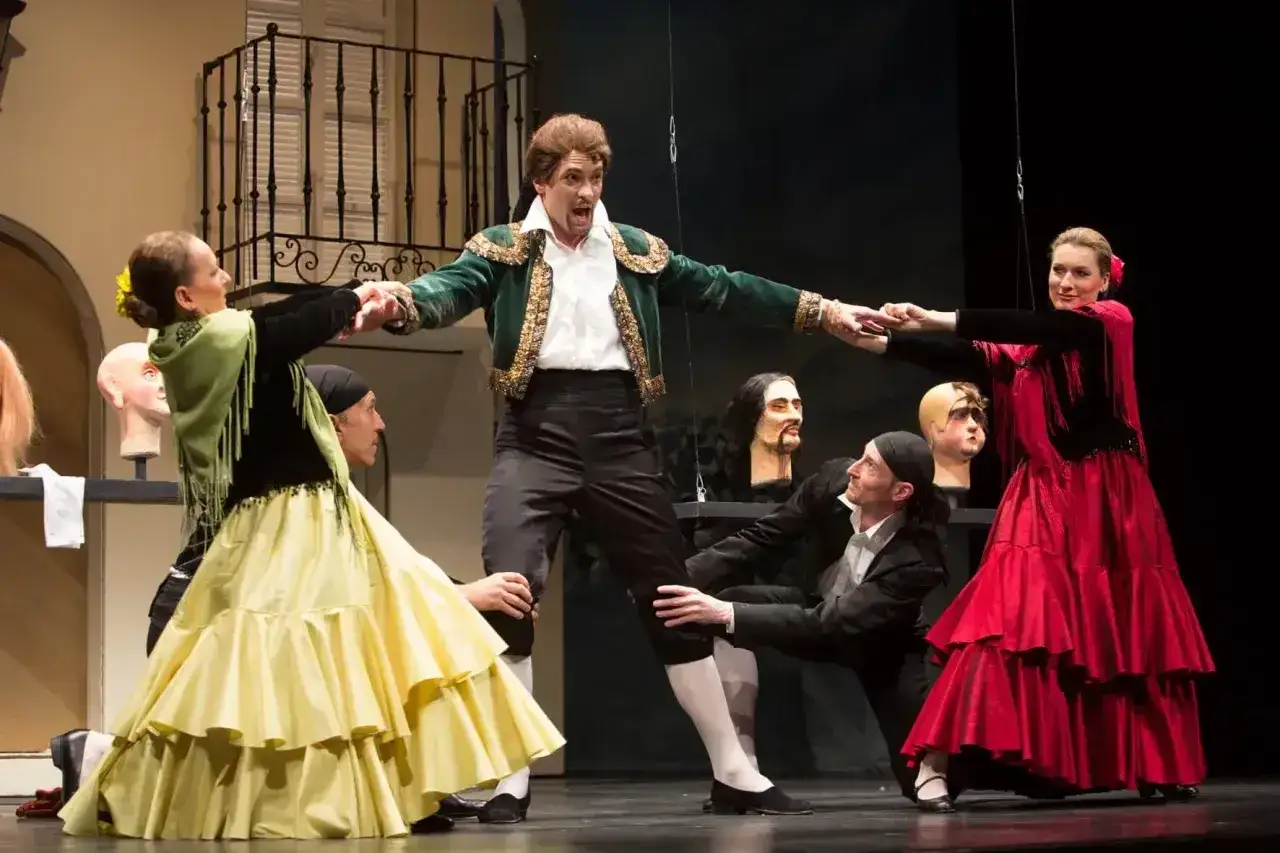 Współcześni polscy śpiewacy operowi w barwnych strojach, w teatralnej scenografii, tworzą dynamiczną scenę.