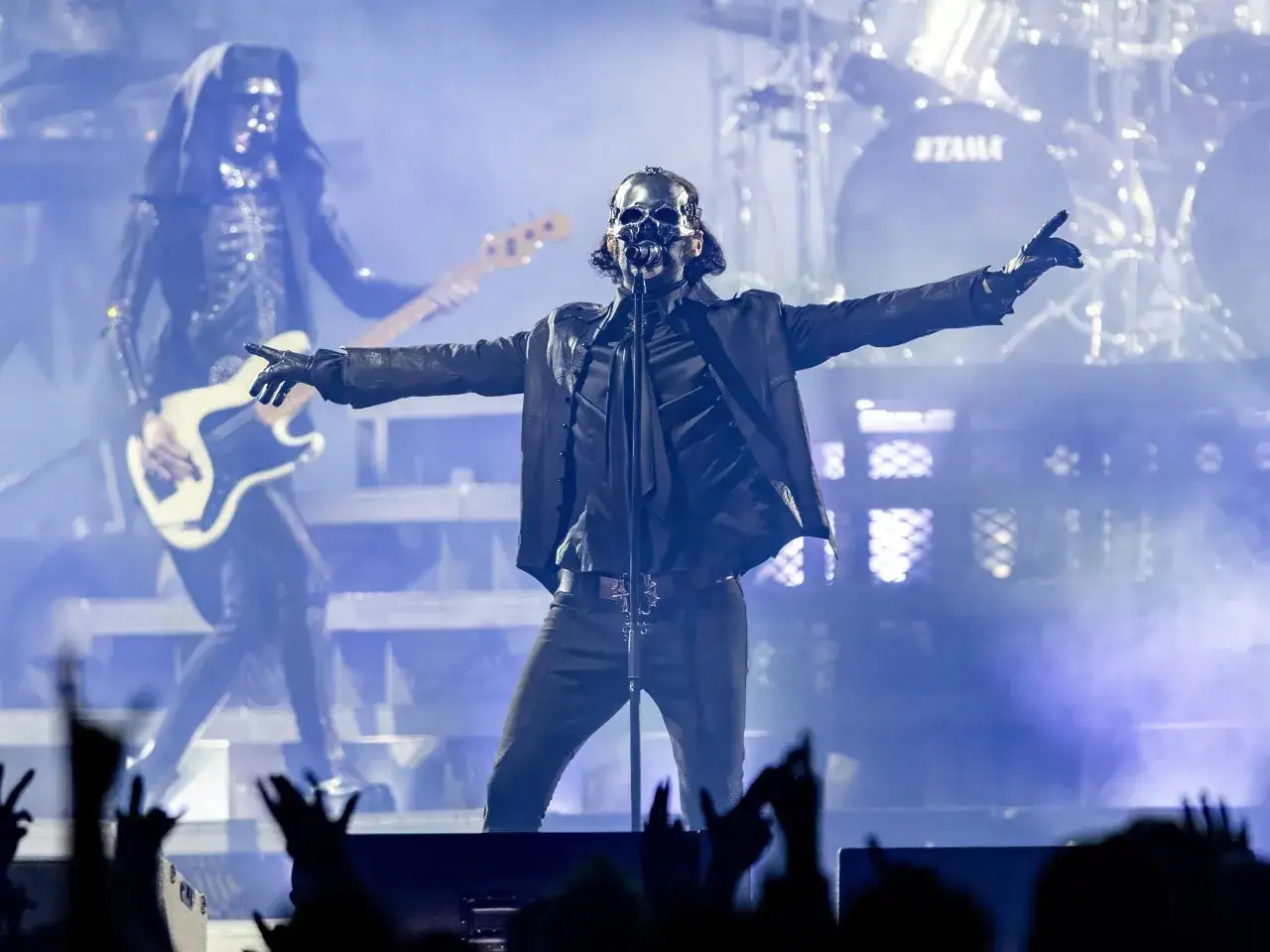 Wokalista w masce czaszki i czarnym stroju, z gitarzystą w tle, podczas koncertu, który mógłby być inspirowany death metalem.