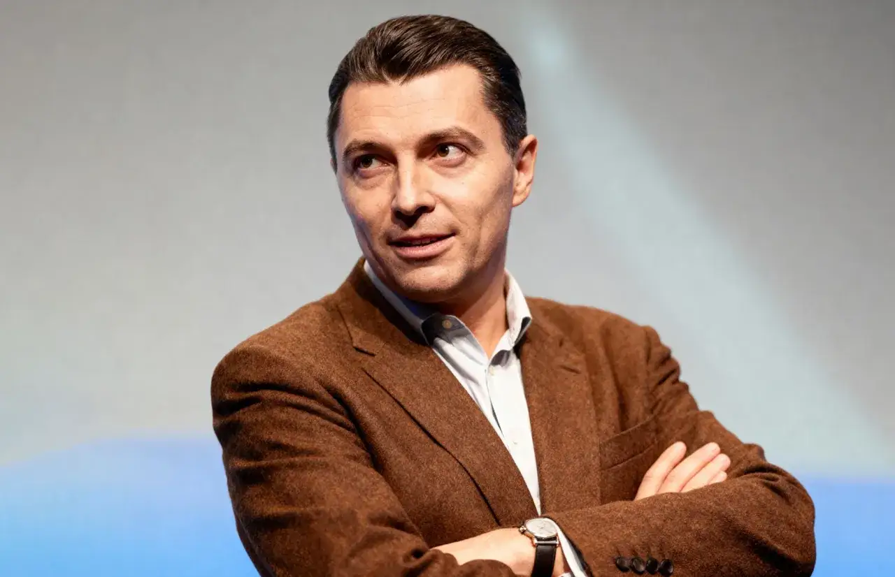 Janusz Budzyński, mąż Alicji Majewskiej, w brązowej marynarce, z rękami skrzyżowanymi na piersi.