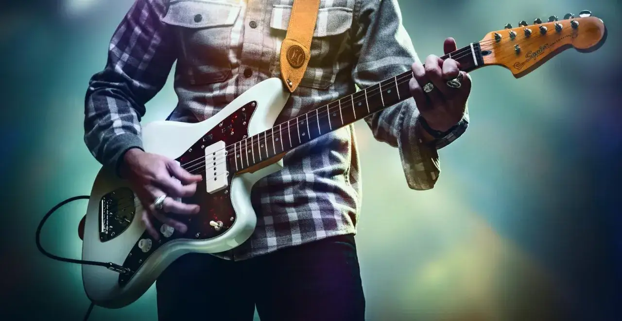 Muzyk w koszuli w kratę gra na białej gitarze, tworząc eteryczne dźwięki w stylu shoegaze.