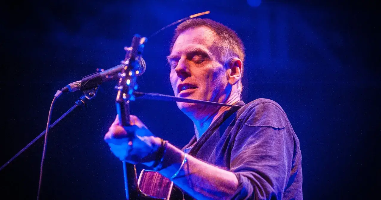 Wokalista zespołu lipińskiego z gitarą na scenie, oświetlony niebieskim światłem.