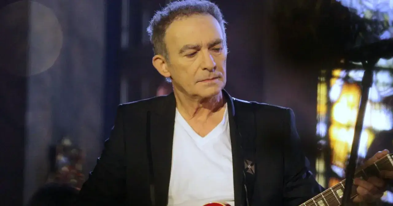 Artysta z gitarą, w czarnej marynarce i białej koszulce. W tle widać rozmyte światła, co może sugerować, że czy Seweryn Krajewski żyje i występuje.