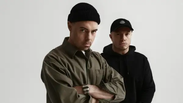 Dwóch mężczyzn, jeden w czarnej czapce beanie i oliwkowej koszuli, drugi w czarnej czapce z daszkiem. Zapowiedź nowych pro8l3m albumy.