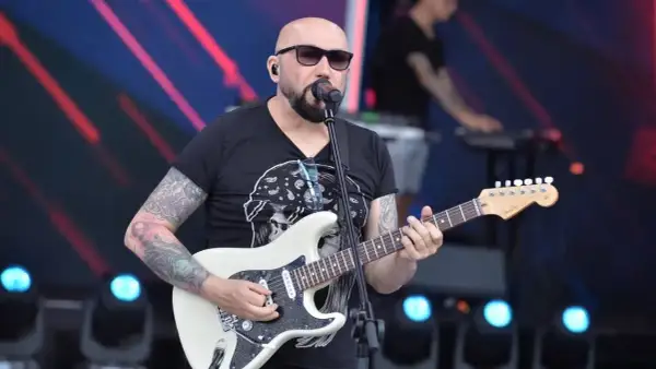 Artysta z tatuażami gra na gitarze, śpiewając do mikrofonu. Koncertowy klimat, jakby to były **kombi piosenki alfabetycznie**.