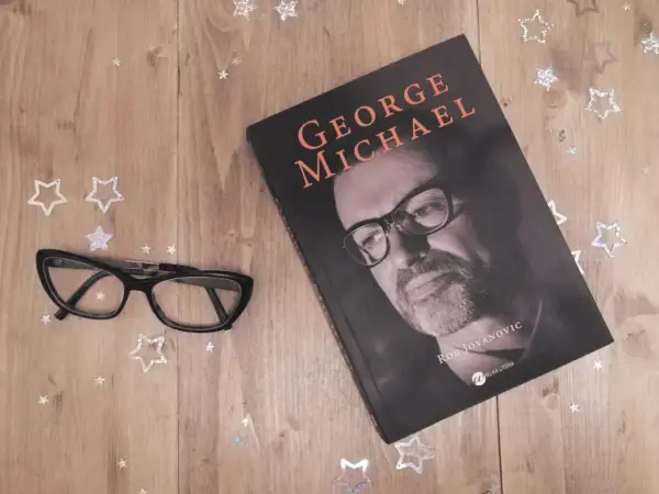 Okładka książki o George'u Michaelu, obok okulary i gwiazdki. Idealna lektura dla fanów jego albumów.