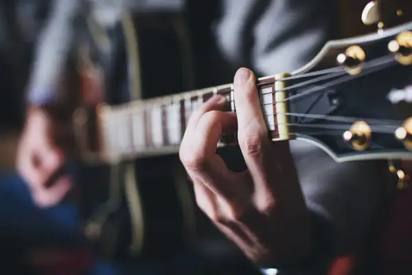 Dłoń grająca akord na gitarze. Muzyka tworzy niepowtarzalny zespół z korą drzewa, z którego wykonano instrument.