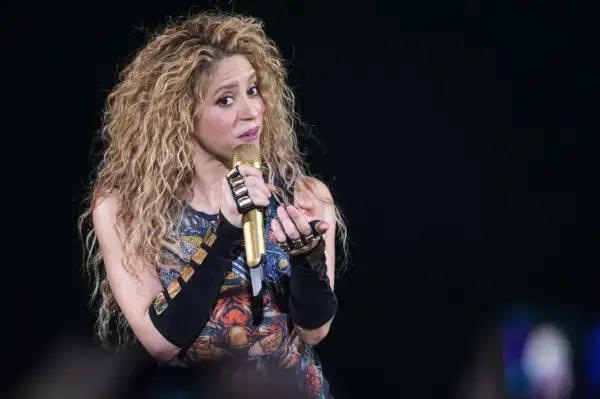 Shakira, znana z latynoskiego pochodzenia, śpiewa na scenie z mikrofonem w dłoni.