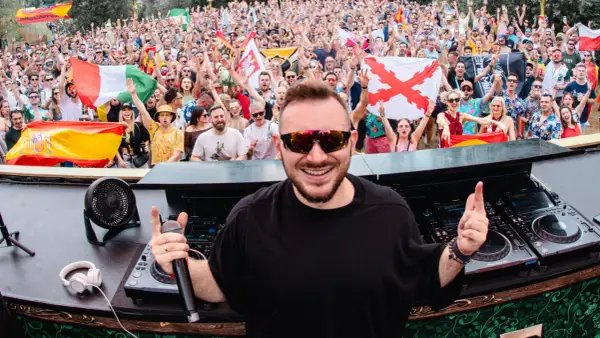 Skytech DJ w akcji, rozkręca tłum na festiwalu. W tle widać flagi i radosnych ludzi.