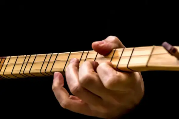 Dłoń na gryfie gitary, palce dociskają struny. Idealny moment, by dowiedzieć się, jak nastroić gitarę.